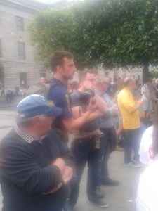 Two Special Branch officers (political police) centre photo in sunglasses -- blue pattern shirt and brown T-shirt top next to him.  There were eight SB identified, all watching the counter-protesters.
