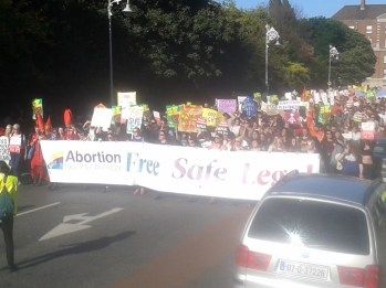 Ag teacht isteach ar thaobh dheis Chearnóg Mhuirfeann (tabhair faoi deara an placárd i nGaeilge sa lár taobh láimhe deise)